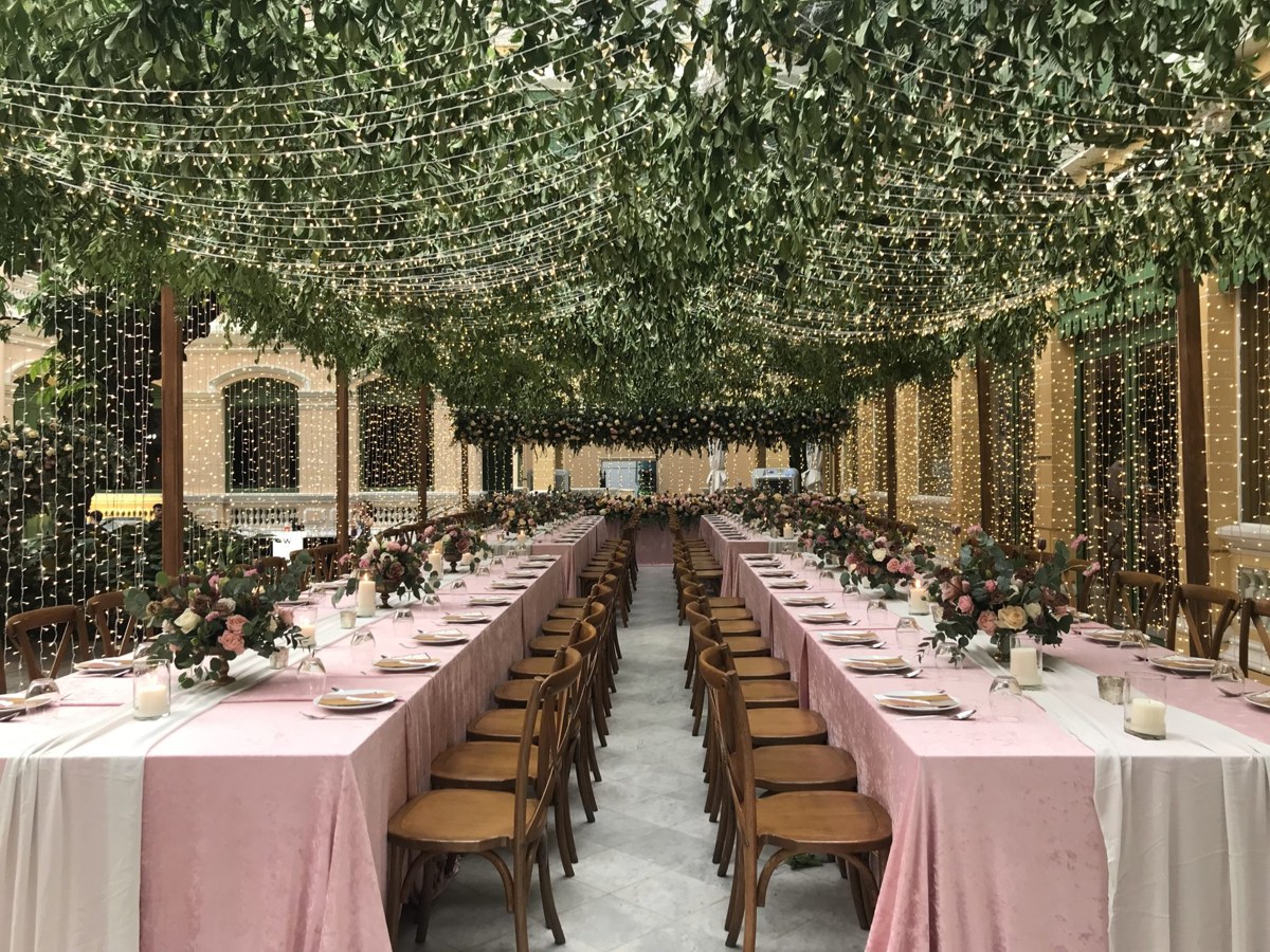 Mesas compridas de casamento sob um teto de verdura e luzes